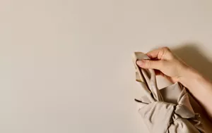 Close up of person's hand tying knot of beige Furoshiki wrapping on top of a beige surface